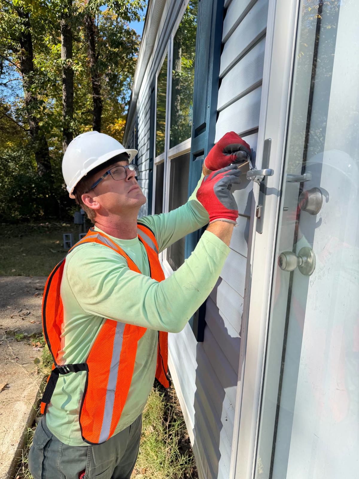 Crew member in a hard hat, glasses, work gloves, and hi-vis vest working on a home's storm door