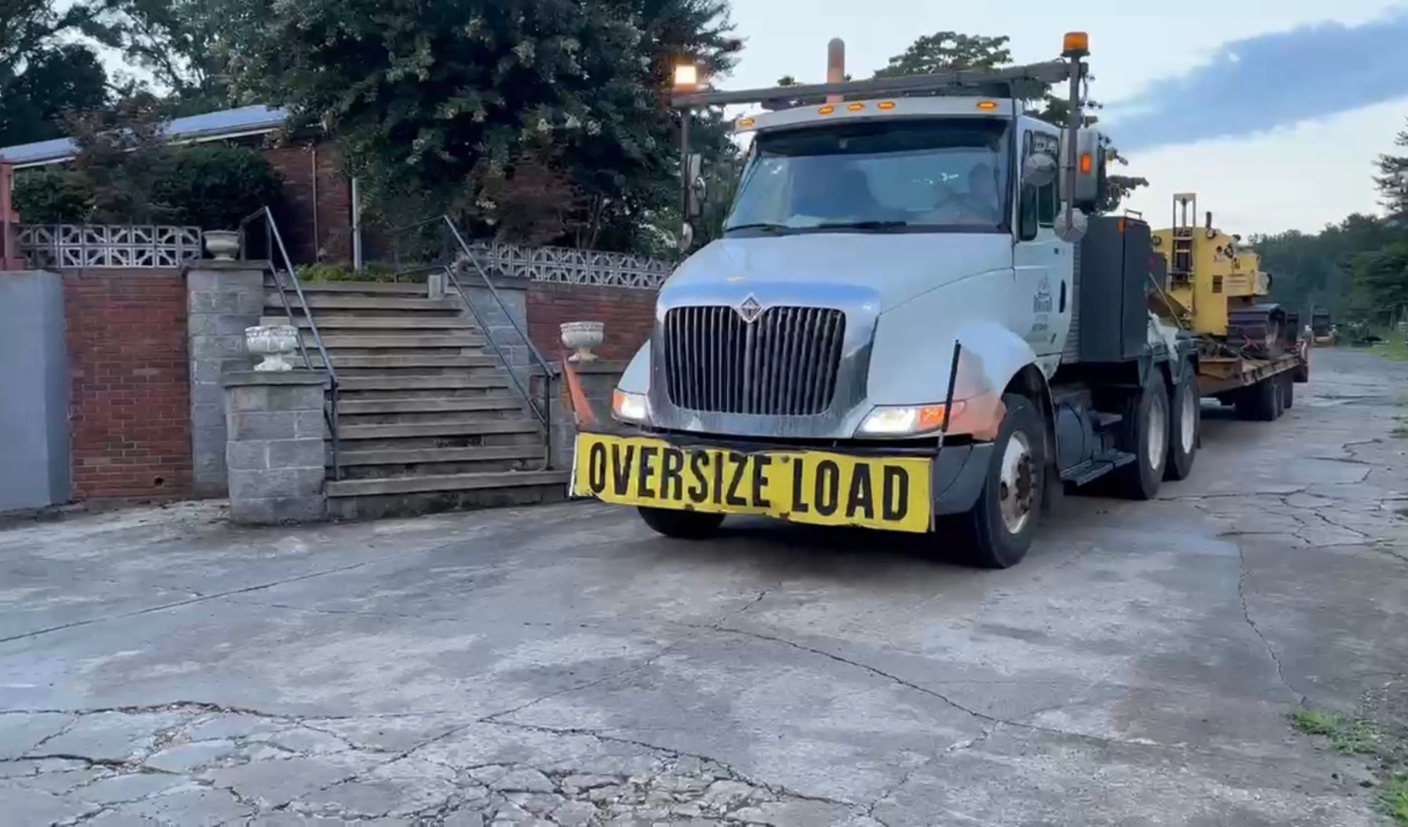Oversize-load truck with amber beacons hauling a house tug on a lowboy trailer