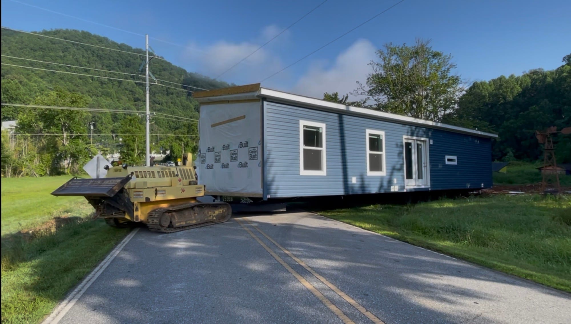 House tug moving a new blue home along a paved road